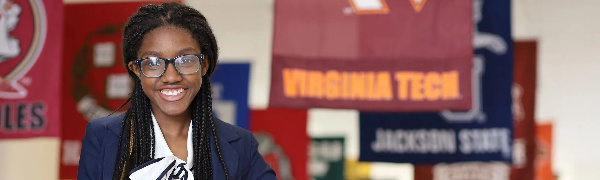 10 A smiling student wearing glasses and a navy blazer stands in front of colorful college banners, including one for Virginia Tech, embodying educational empowerment and the promise of education.