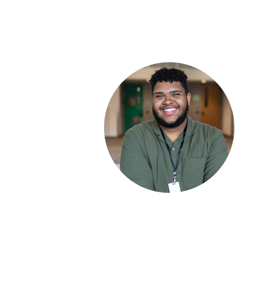 A man with short curly hair and a beard, wearing a green shirt and a lanyard, smiles while standing in a hallway—reflecting educational empowerment against blurred doors. The circular image is set on a light gray background.