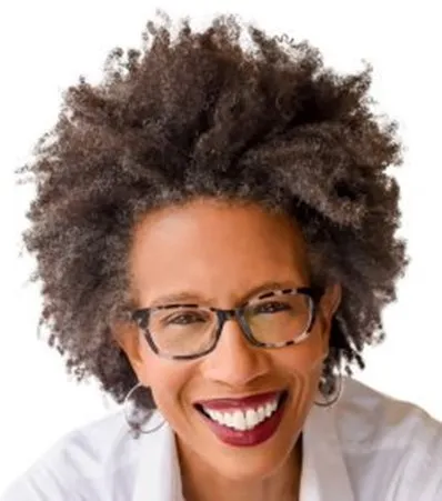 A smiling woman with curly, dark hair, wearing glasses, hoop earrings, and a white shirt, set against a white background.